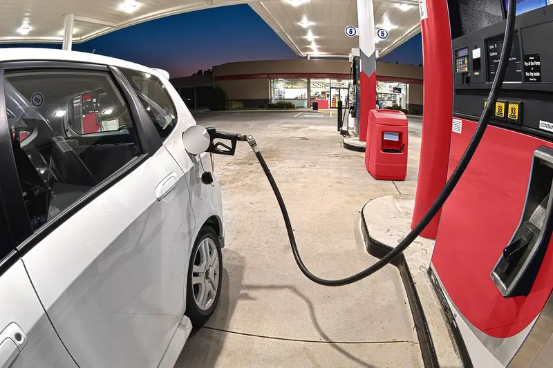 A car at the pump of a filling station at dusk, the store lit behind it.