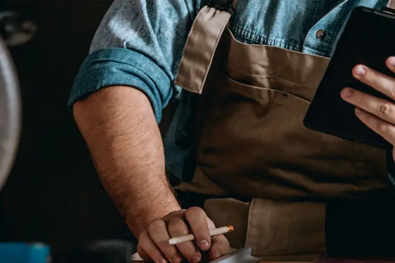 A workshop owner in an apron costing a job on a tablet, pencil in hand.