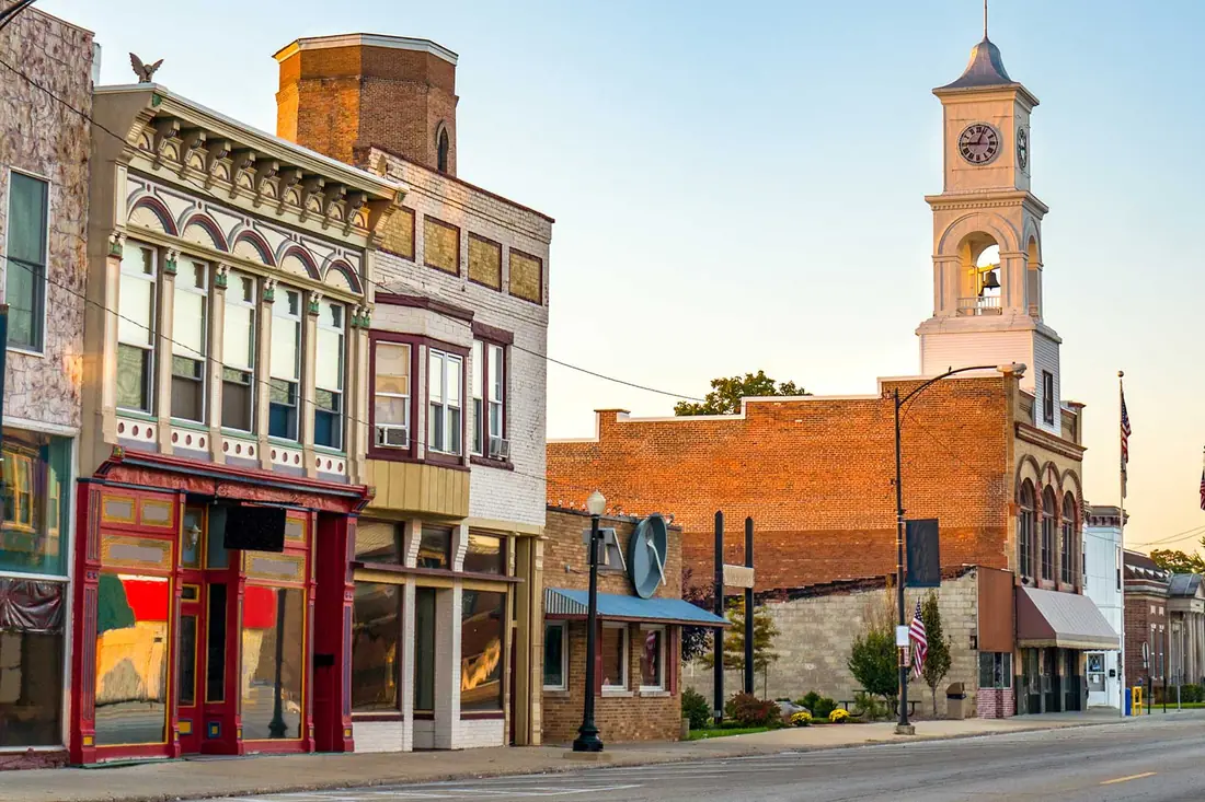 A main street of independent shops under a clock tower, early in the morning.